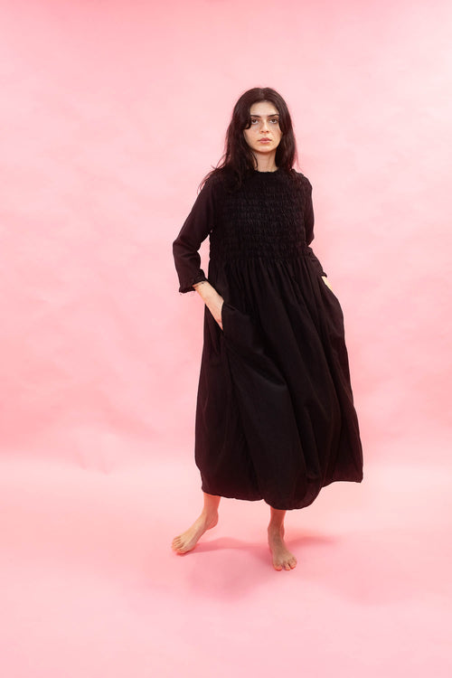 Woman wearing a black loose fit midi dress against a pink background