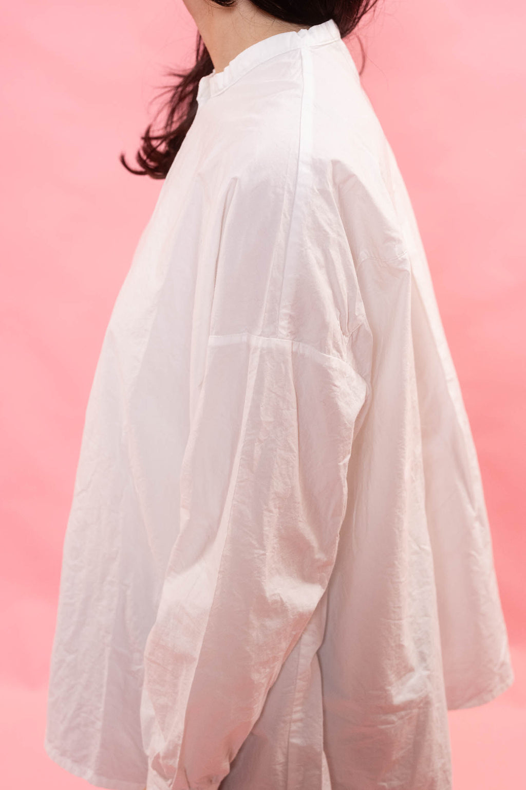 A person wearing an oversized white long-sleeve shirt, shown from the side against a solid pink background.