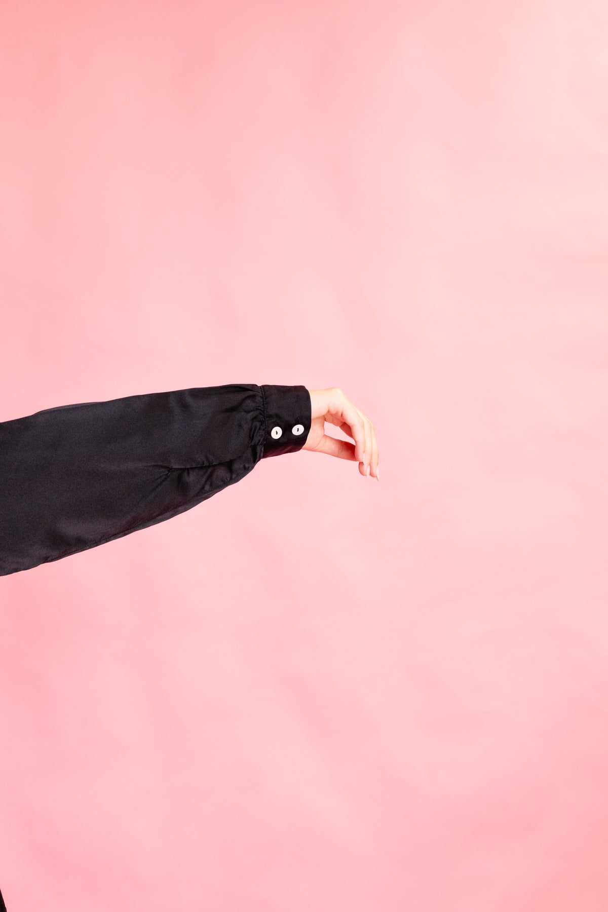 Cuff detail of a black silk shirt and a mother of pearl button fastening