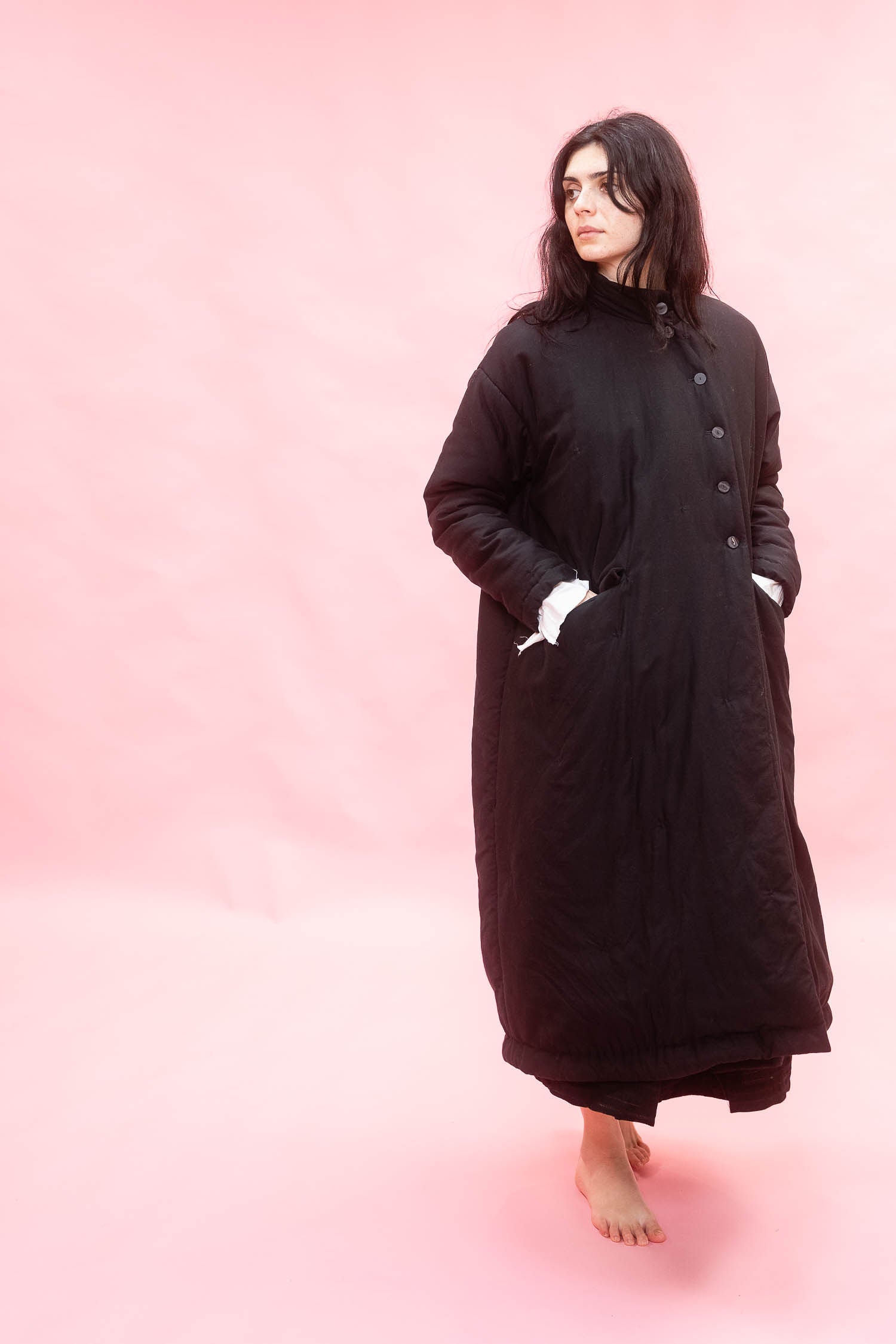 Woman wearing a long black coat on a pink background