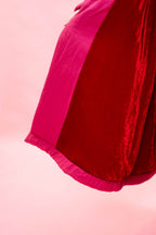 A close-up of the cuddle coat in two contrasting colours: a deep red velvet lining and a bright hot pink silk satin outer, set against a solid light pink background.