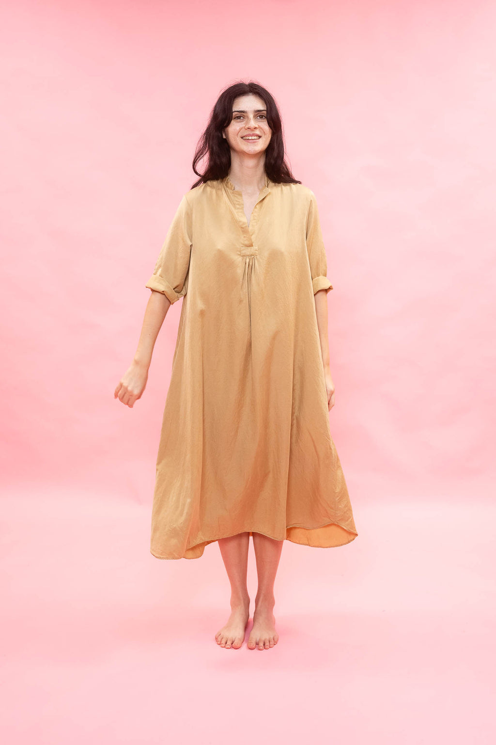 Woman wearing a beige dress against a pink background
