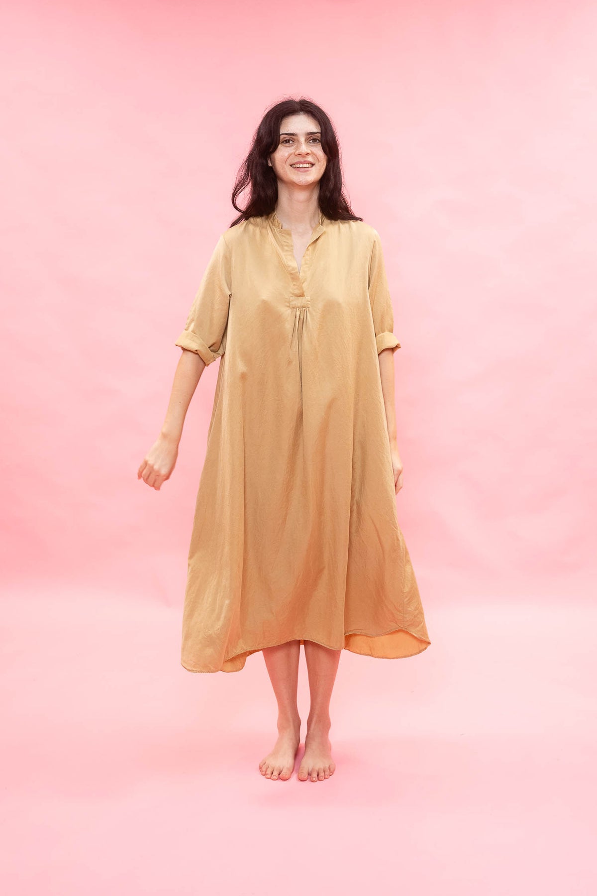 Woman wearing a beige dress against a pink background