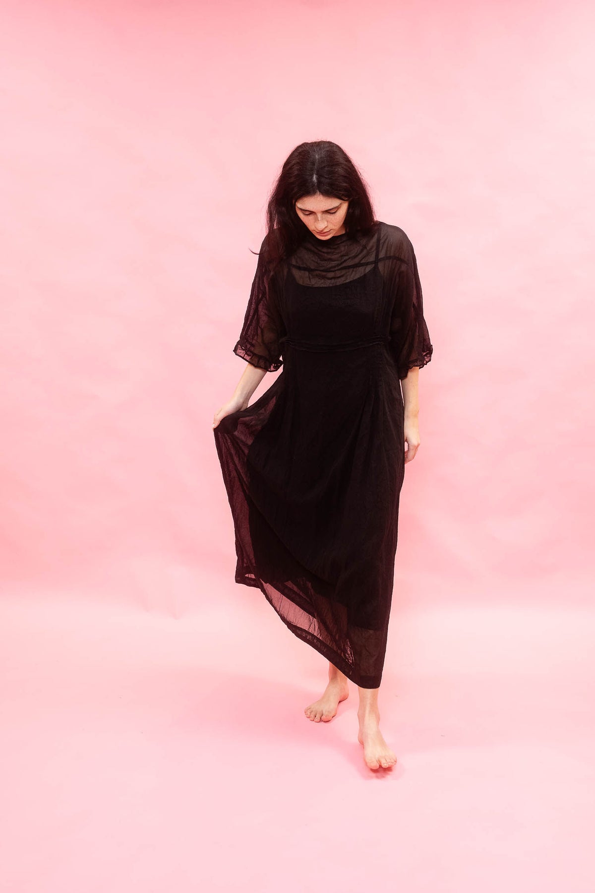 Woman wearing a black dress with sheer sleeves against a pink background