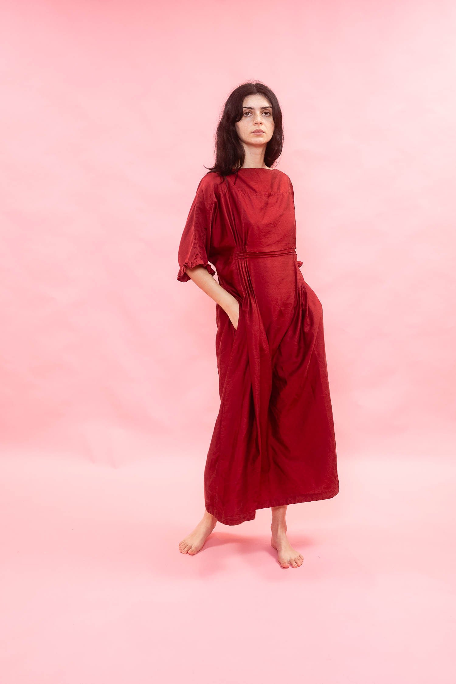 Woman wearing a midi length silk satin red dress against a pink background