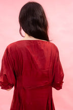 A woman viewed from behind wearing a deep red long-sleeve dress against a solid pink background.