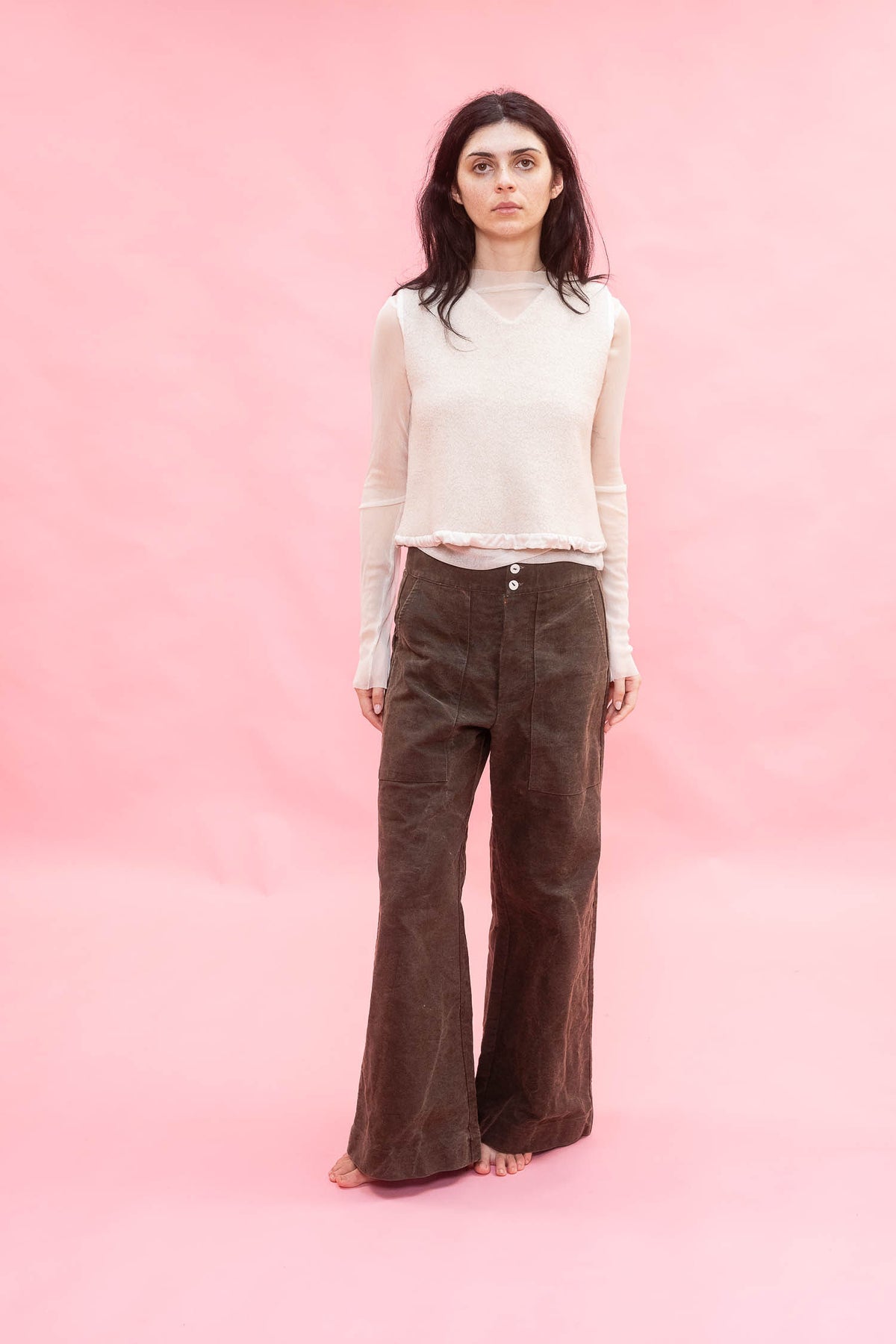 Woman wearing a white top and brown pants against a pink background