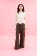 Woman wearing a white top and brown cotton wide leg 
pants against a pink background
