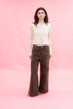 Woman wearing a white top and brown cotton wide leg 
pants against a pink background