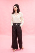 Woman wearing a cream cotton japanese Organdy blouse and dark pants on a pink background
