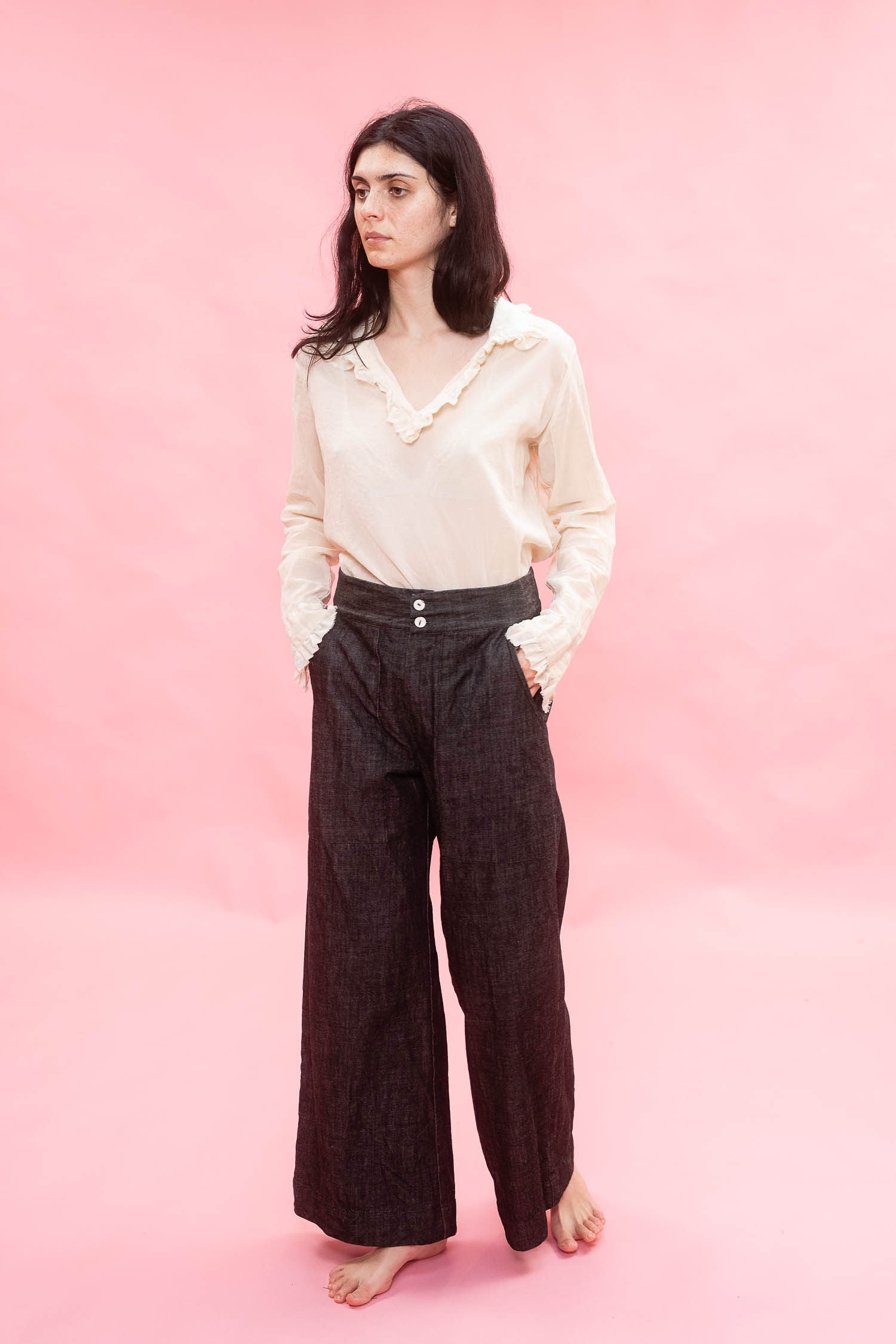 Woman wearing a cream cotton japanese Organdy blouse and dark pants on a pink background
