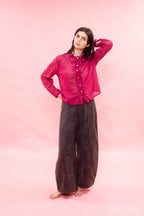 Person wearing a pink sheer blouse and brown pants on a pink background
