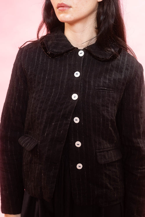 A close-up of a person wearing a dwool stripe jacket with a wide collar and white buttons, and contrast brown velvet trim on collar set against a solid pink background.