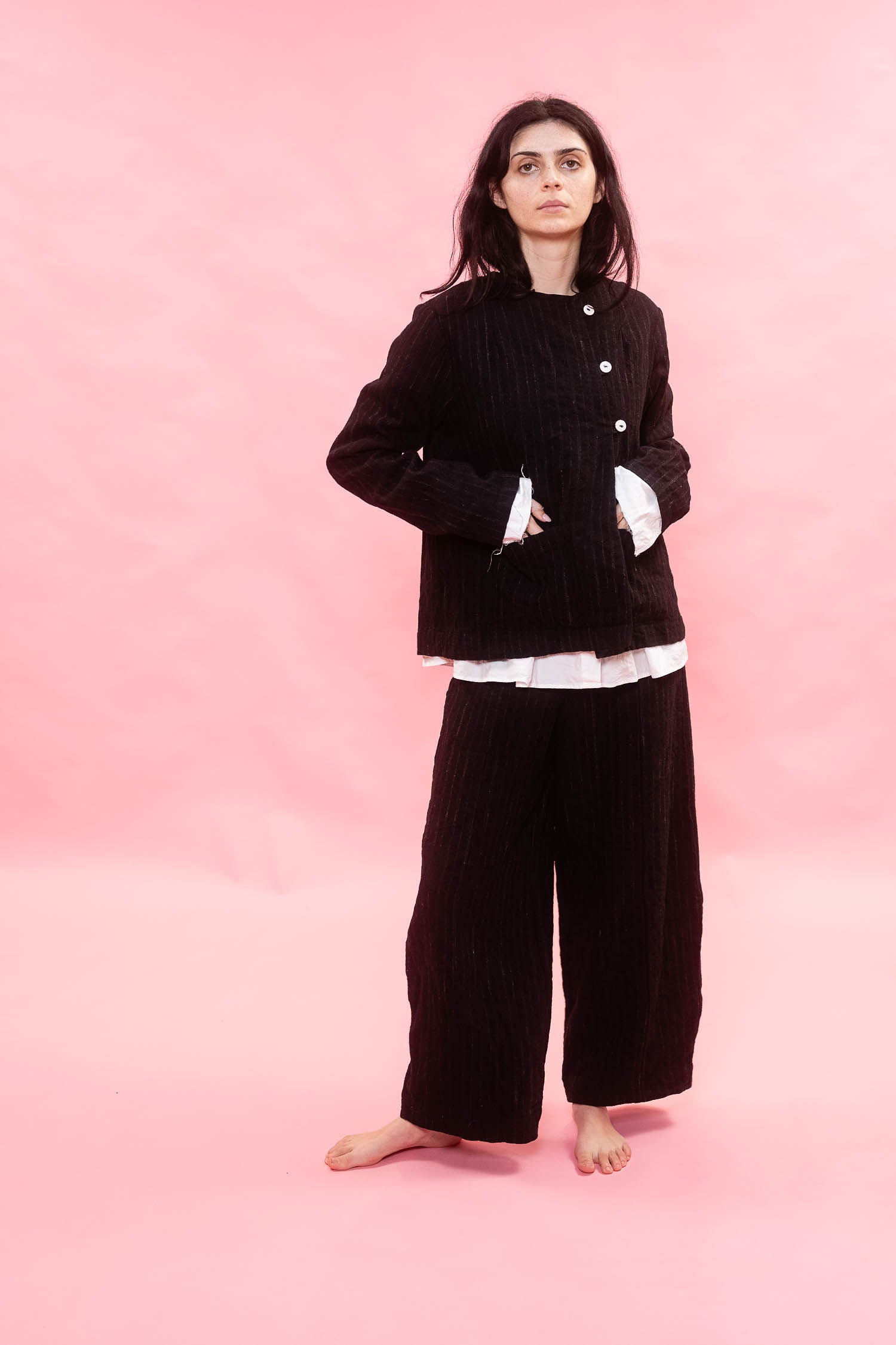 Person wearing a black wool pinstripe jacket with white buttons on a pink background