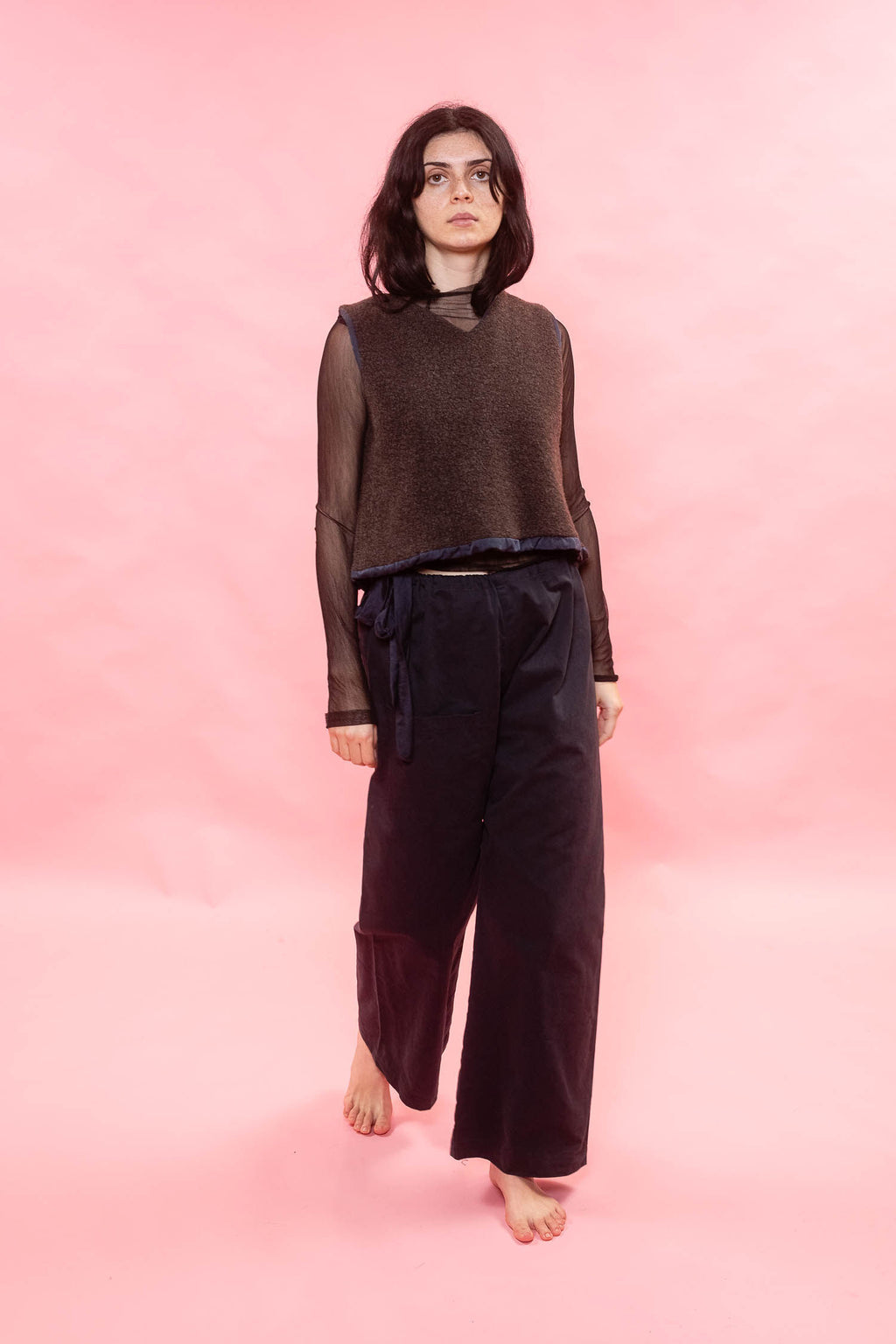 Person wearing a brown top and dark pants on a pink background