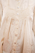 Close-up of a l cream-colored long-sleeve , satin blouse with a pleated bodice, decorative neckline, and a vertical button placket with white buttons.
