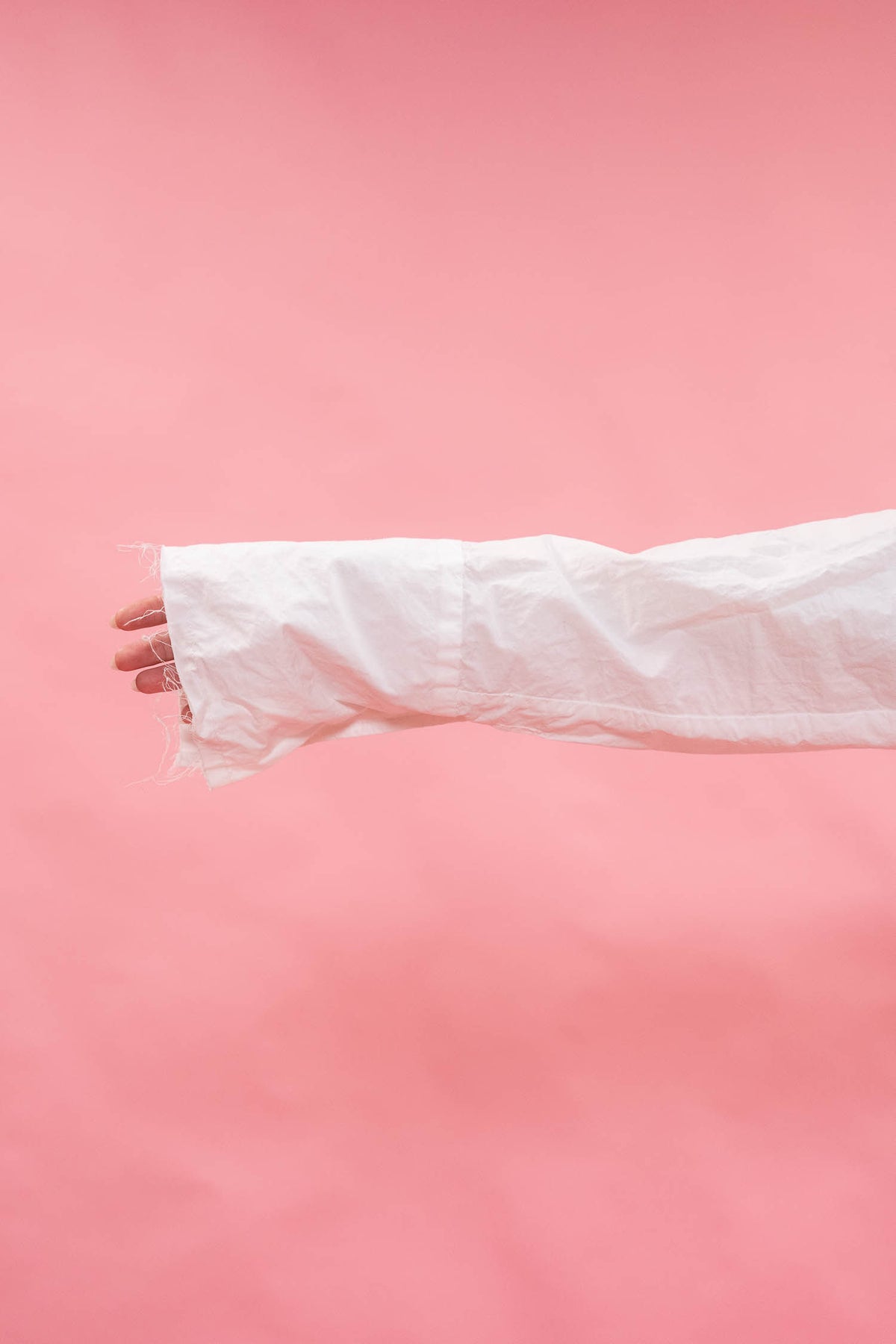 A close-up of a person's hand and forearm wearing a long, oversized white sleeve or cuff, set against a solid pink background.