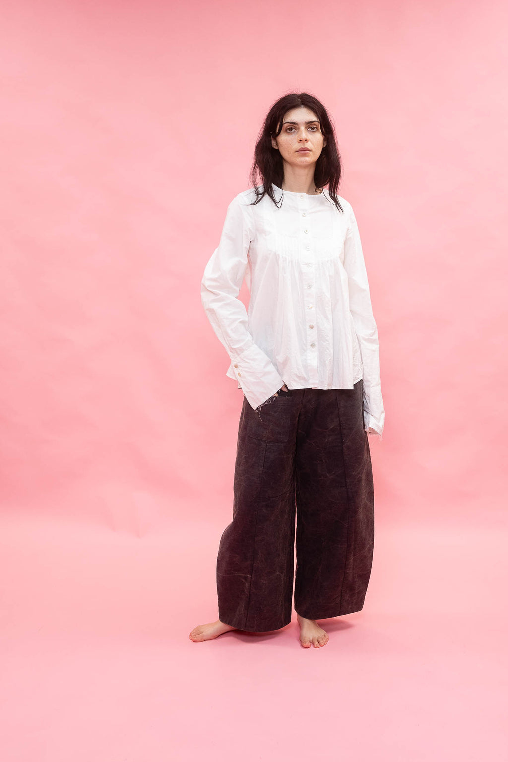 Person wearing a white shirt and dark pants on a pink background