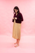 Woman wearing a plum fluffy alpaca knit cardigan over a beige dress on a pink background
