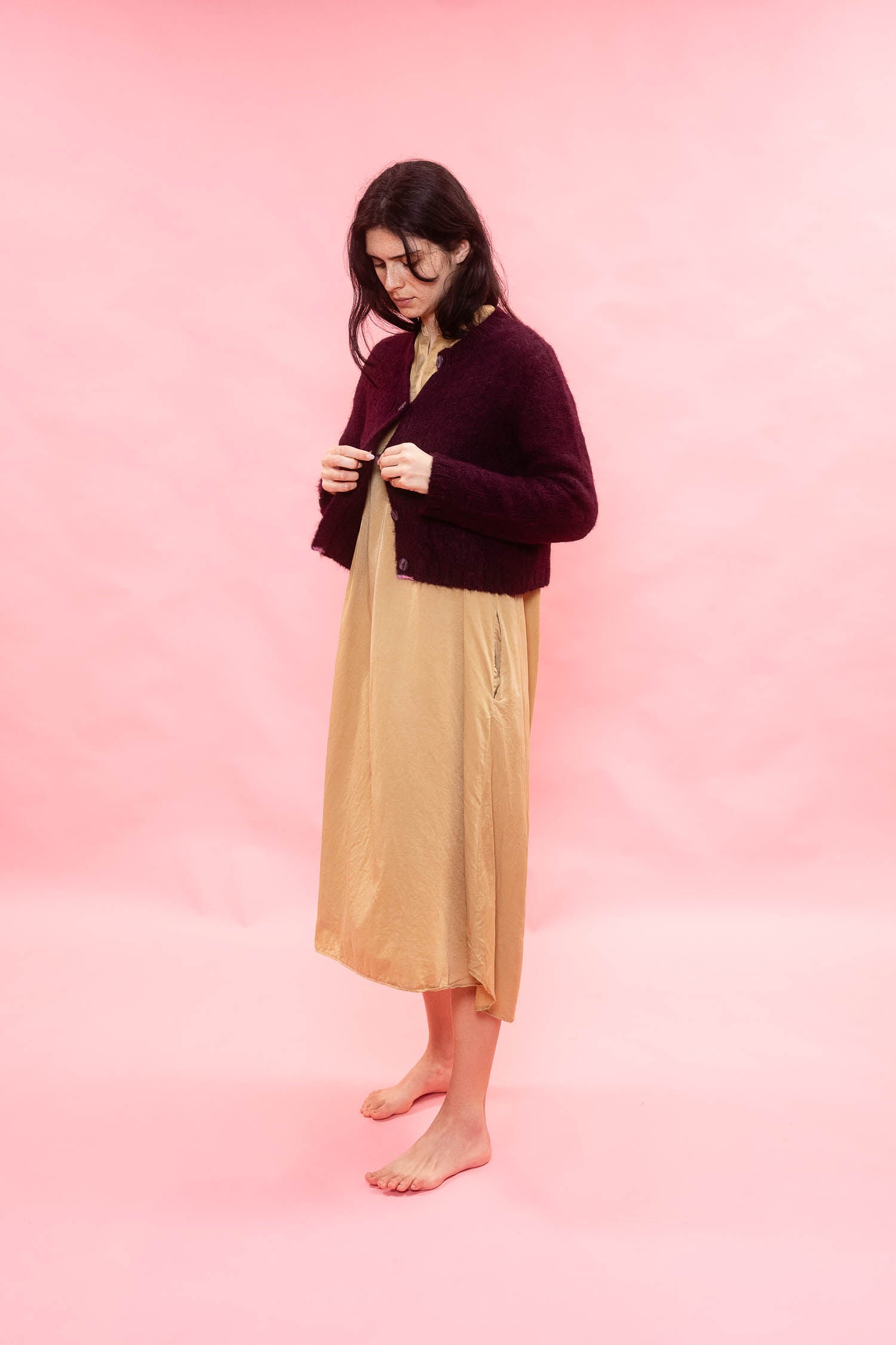 Woman wearing a plum fluffy alpaca knit cardigan over a beige dress on a pink background
