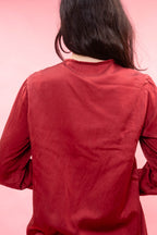 A person viewed from behind wearing a long-sleeve red top against a solid pink background.