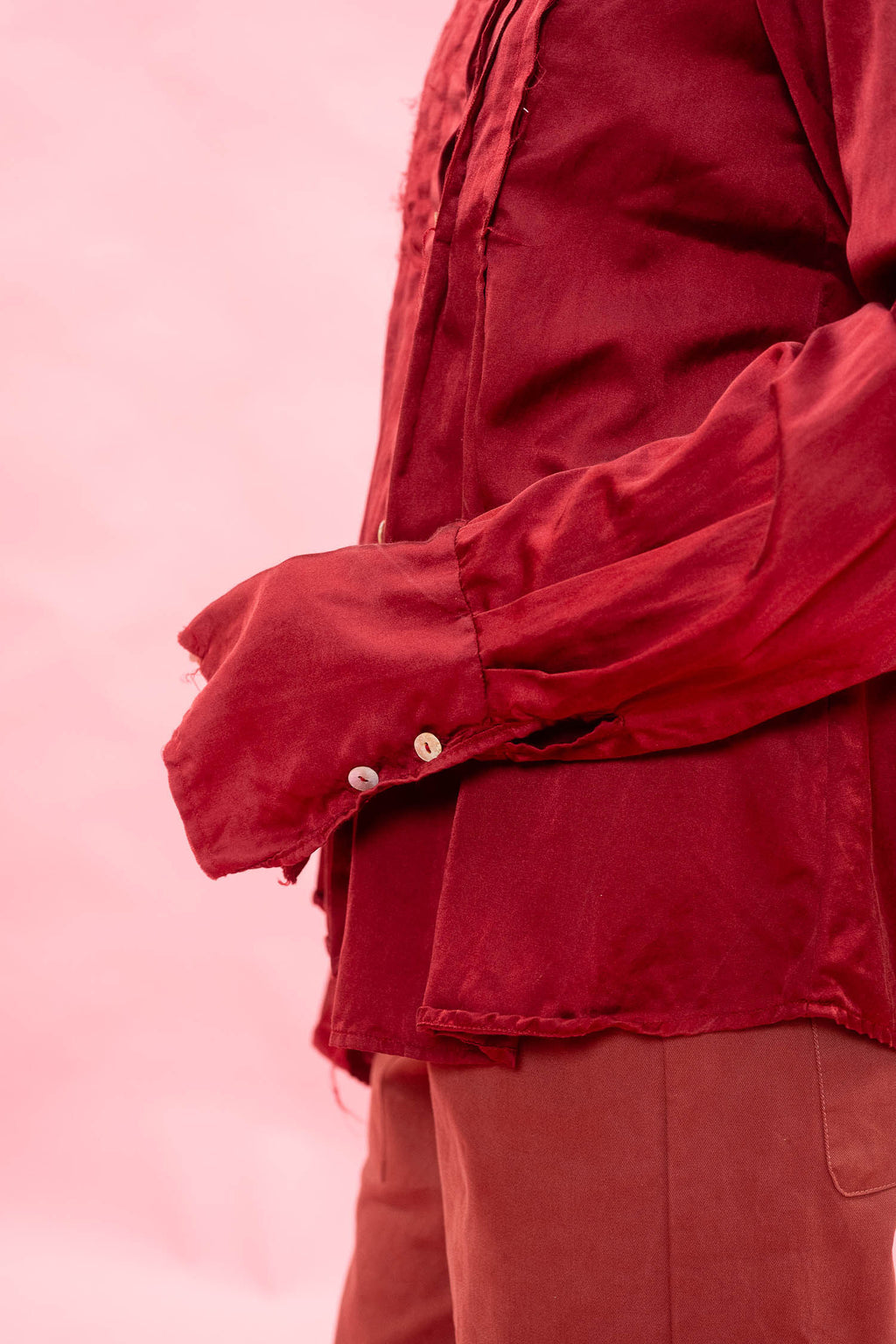 A close-up of a person wearing a long-sleeve red button-up shirt and matching red pants against a soft pink background.