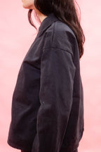 A side-profile view of a person wearing a dark charcoal gray jacket against a solid pink background.