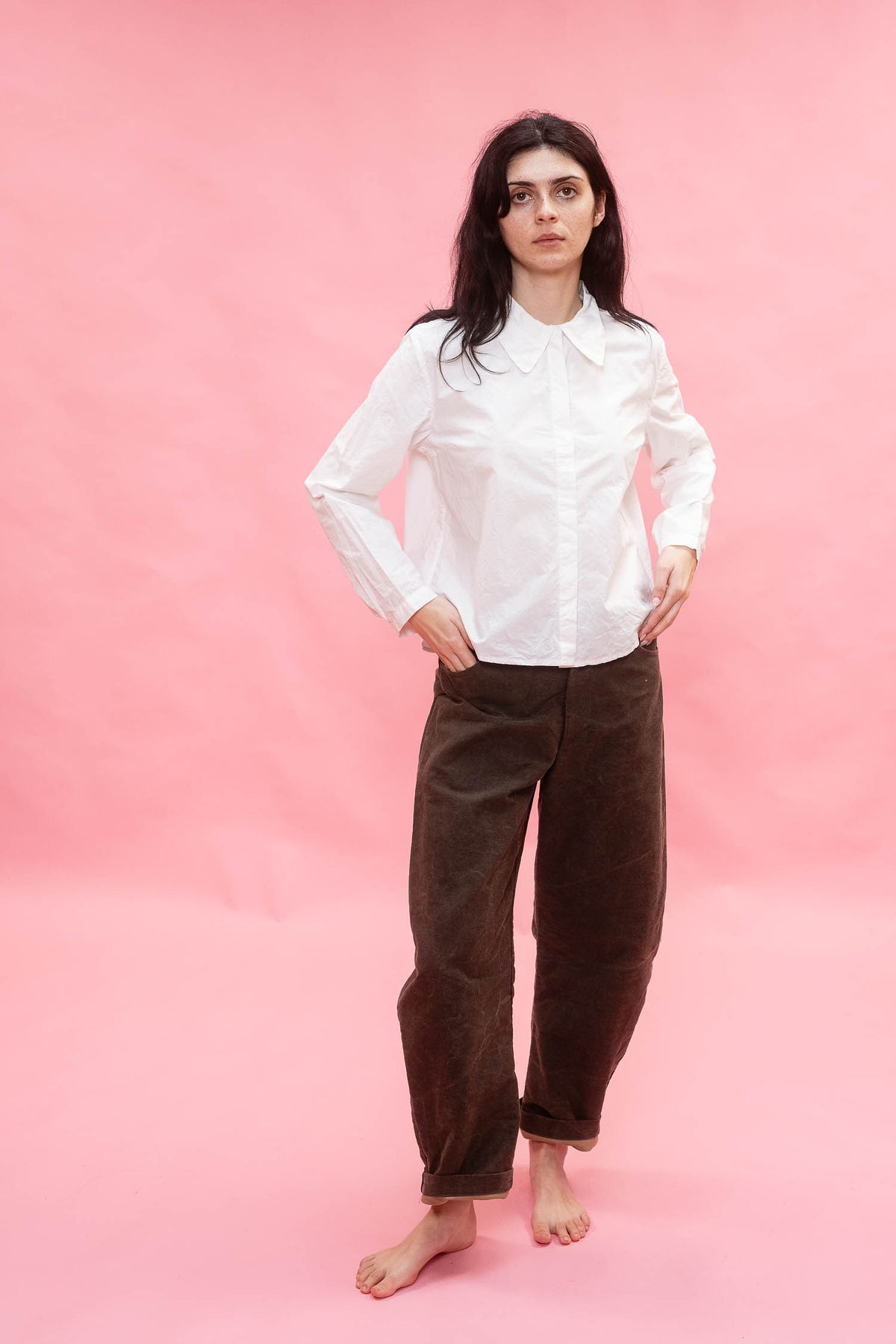 Woman wearing a white blouse and brown pants on a pink background