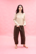 Woman wearing a beige shirt and dirt green brown pants on a pink background