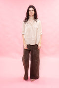 Woman wearing a beige blouse and brown pants against a pink background