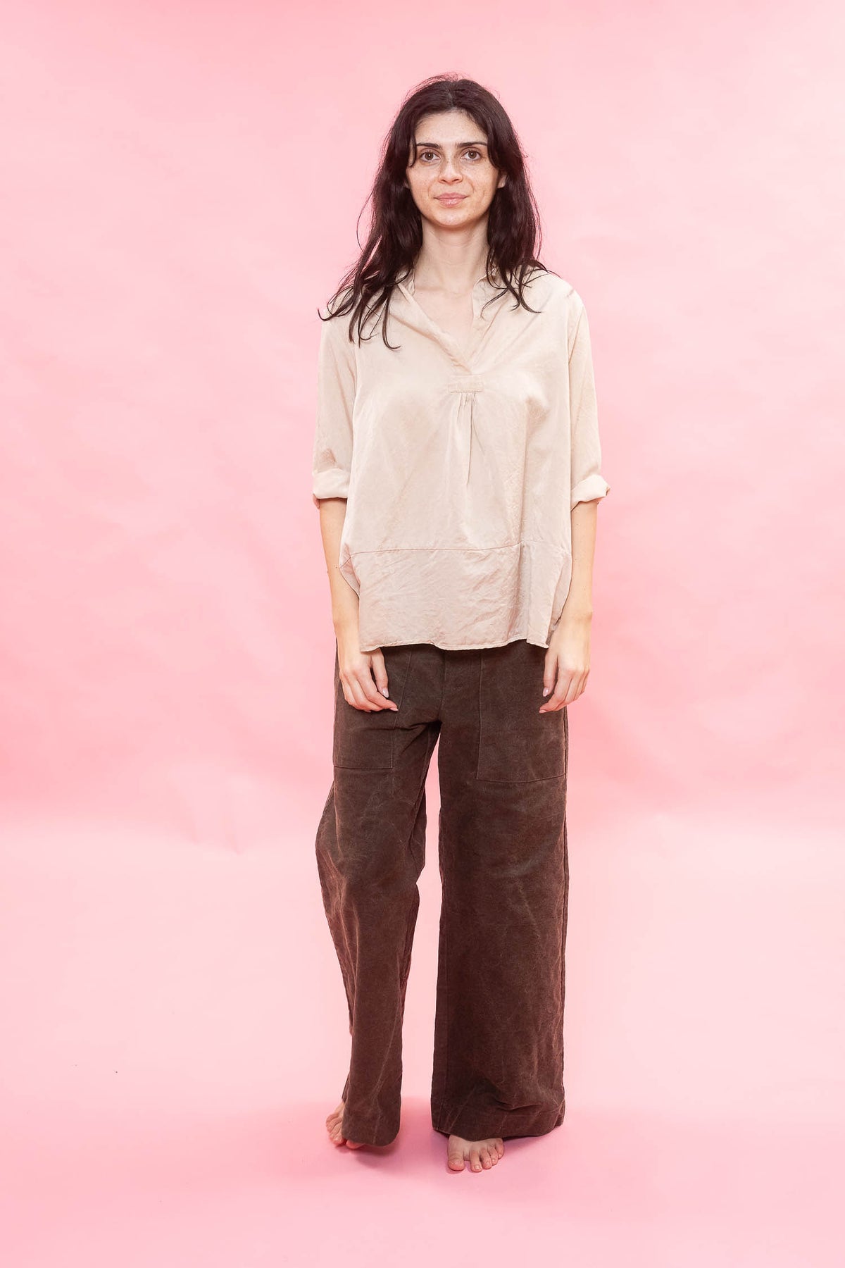 Woman wearing a beige blouse and brown pants against a pink background