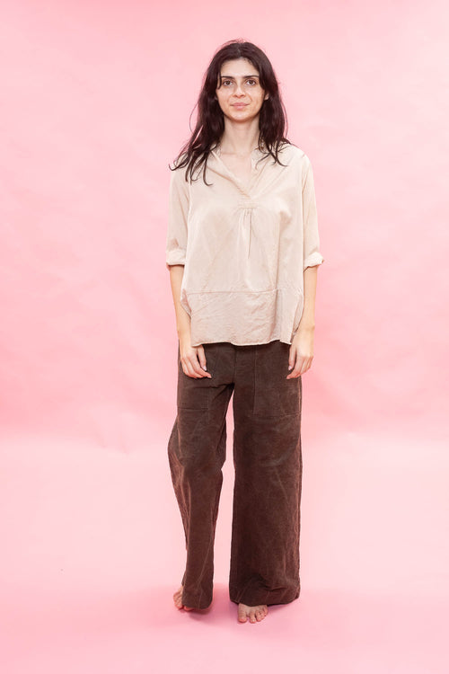 Woman wearing a beige blouse and brown pants against a pink background