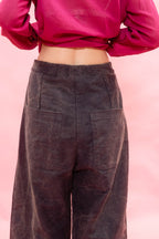 A person shown from the back wearing dark charcoal wide-leg trousers with large patch pockets and a bright pink cropped long-sleeve top, against a solid pink background.
