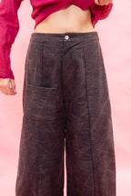 A person wearing dark brown wide-leg corduroy pants with a button waistband and front patch pocket, paired with a magenta cropped top, against a solid pink background.