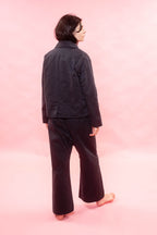A person shown from the back wearing a navylong-sleeve cropped jacket and matching wide-leg pants, standing barefoot against a solid pink studio background.