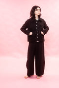 A woman wearing a black broken pinstripe button front jacket and widely pants outfit on a pink background