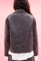 A person shown from the back wearing a grey textured jacket over a white shirt, set against a solid pink background.