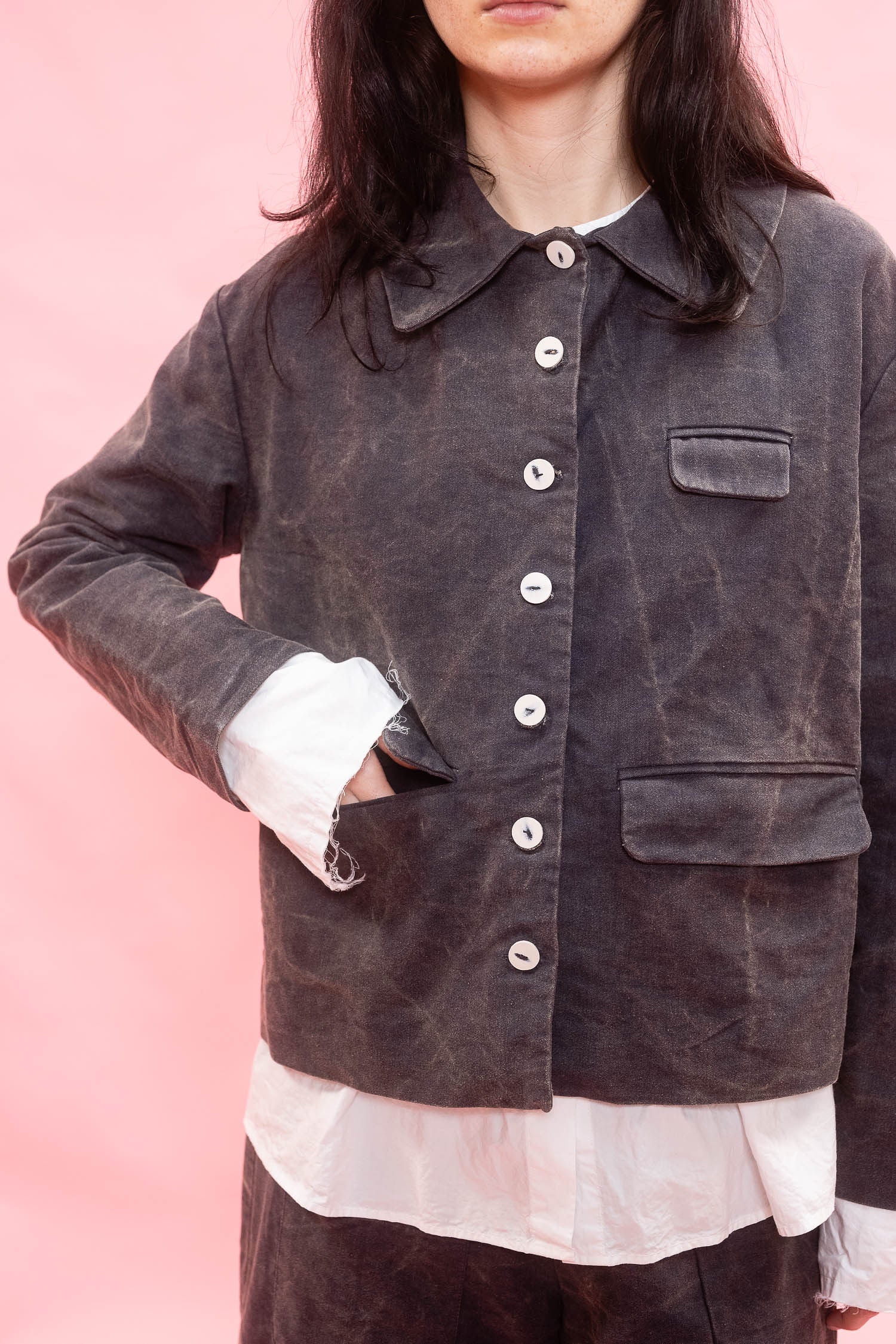 A person wearing a dark washed button-front jacket over a white shirt, photographed against a solid pink background.