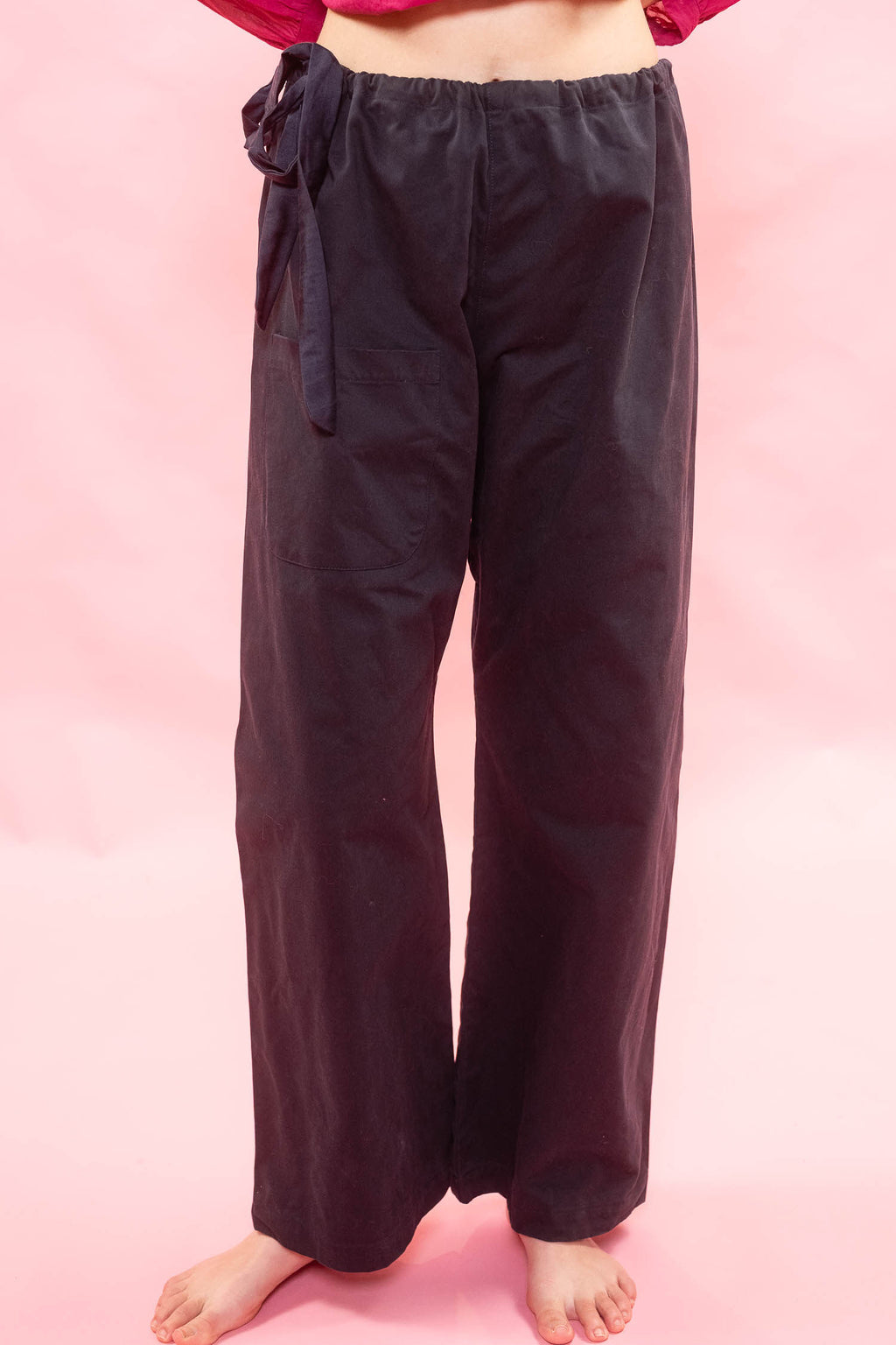 Navy wide-leg pants with a drawstring waist, worn by a model standing against a pink background.