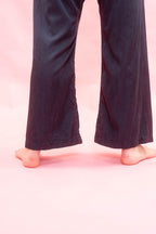 A person's bare feet and lower legs wearing dark navy wide-leg pants against a solid pink background.