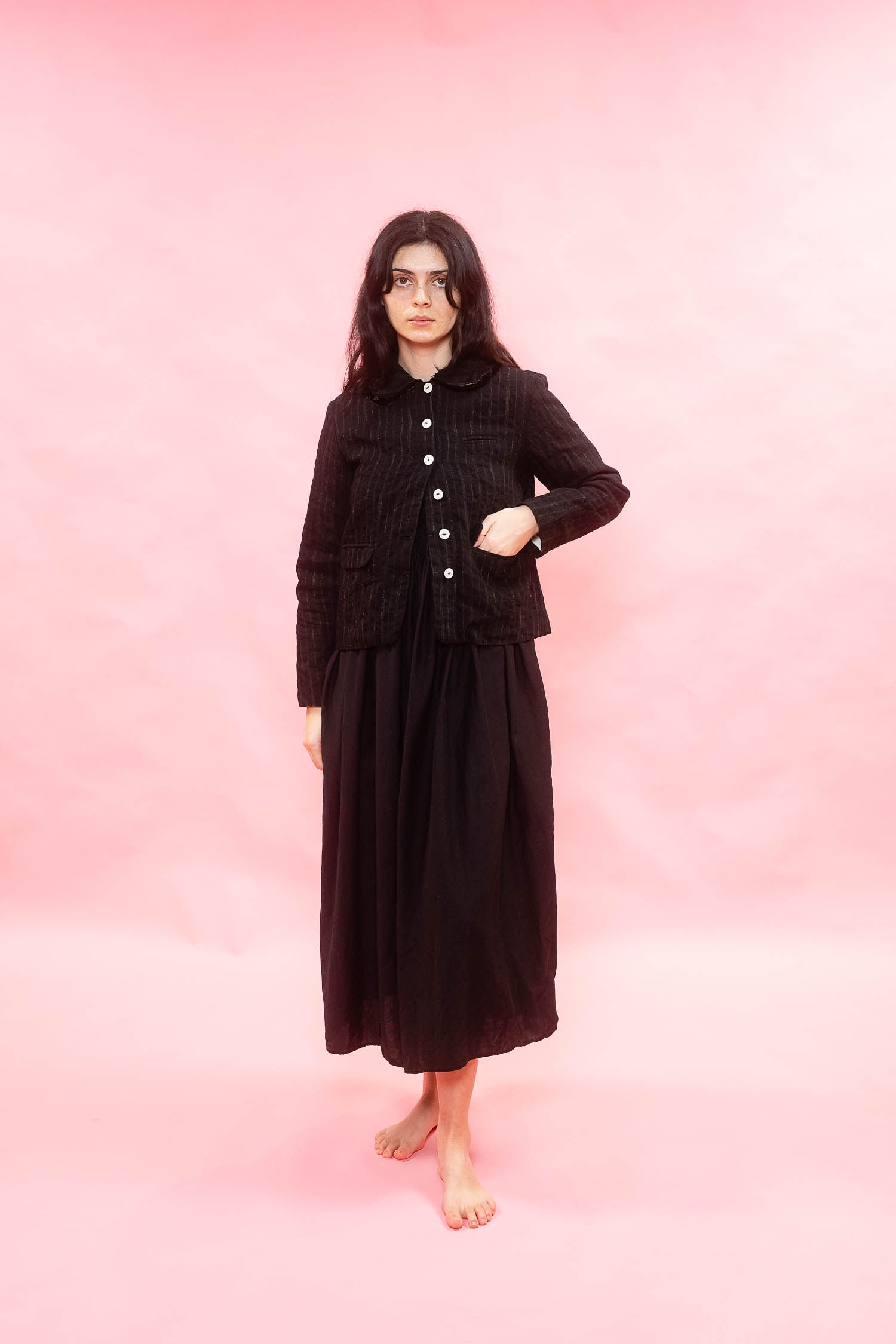 Person wearing a black pinstripe wool jacket and skirt on a pink background