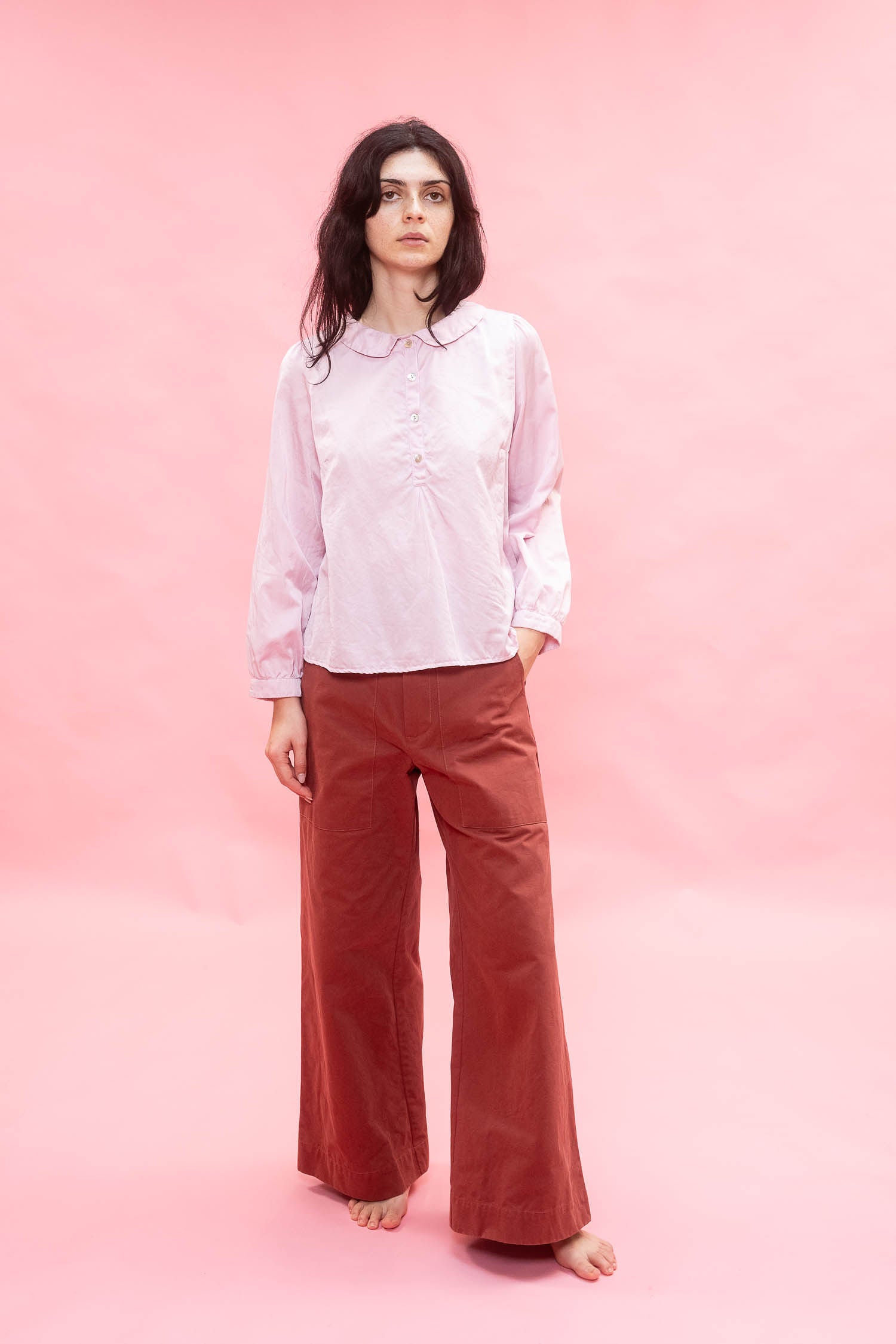 Person wearing a light pink silk cotton satin shirt and rust-colored pants on a pink background