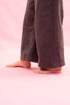 A close-up of a person's bare feet and lower legs wearing dark navy wide-leg linen pants against a solid pink background.