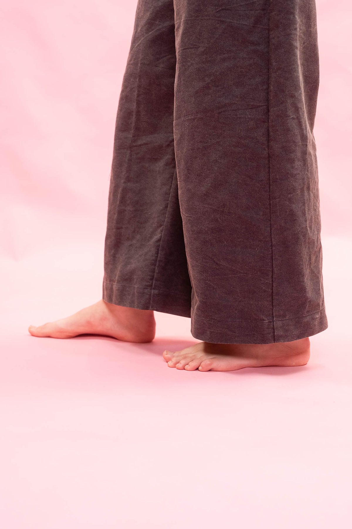 A close-up of a person's bare feet and lower legs wearing dark navy wide-leg linen pants against a solid pink background.